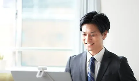 パソコンに向かって微笑むスーツ姿の男性