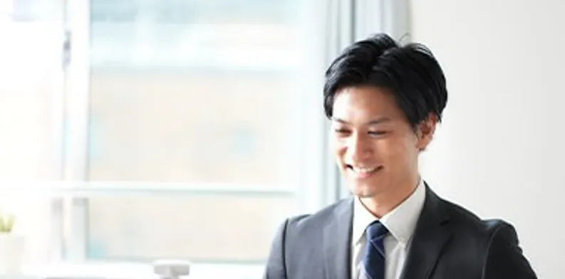 パソコンに向かって微笑むスーツ姿の男性
